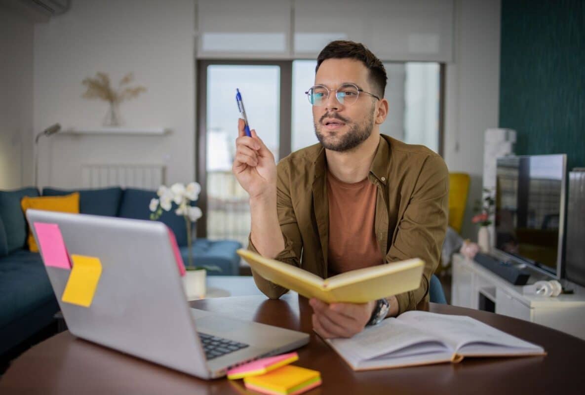 Young man studying English online at home desk with laptop, notebook, and pen—ideal for Anat Megidlor's virtual lessons.