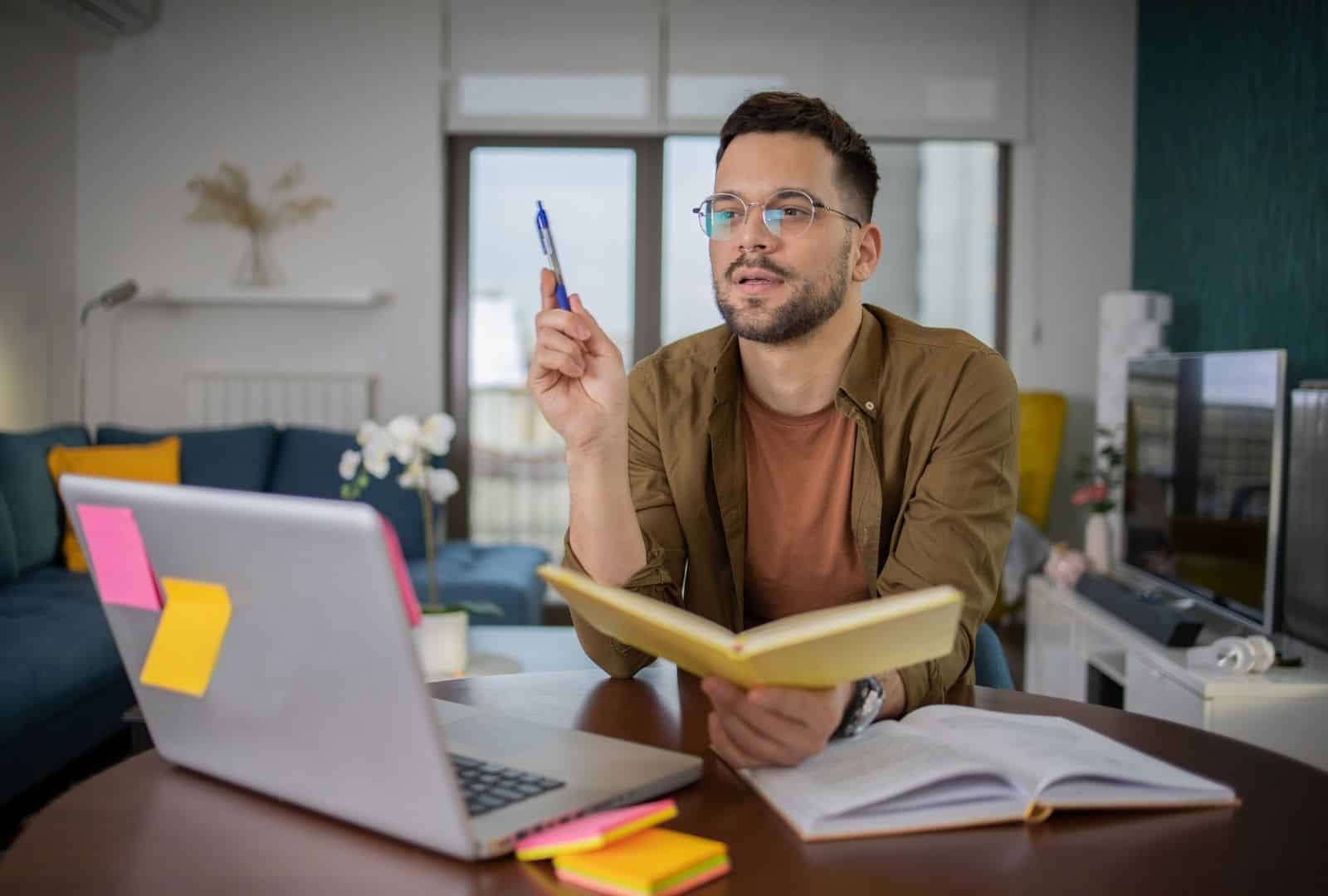 Young man studying English online at home desk with laptop, notebook, and pen—ideal for Anat Megidlor's virtual lessons.