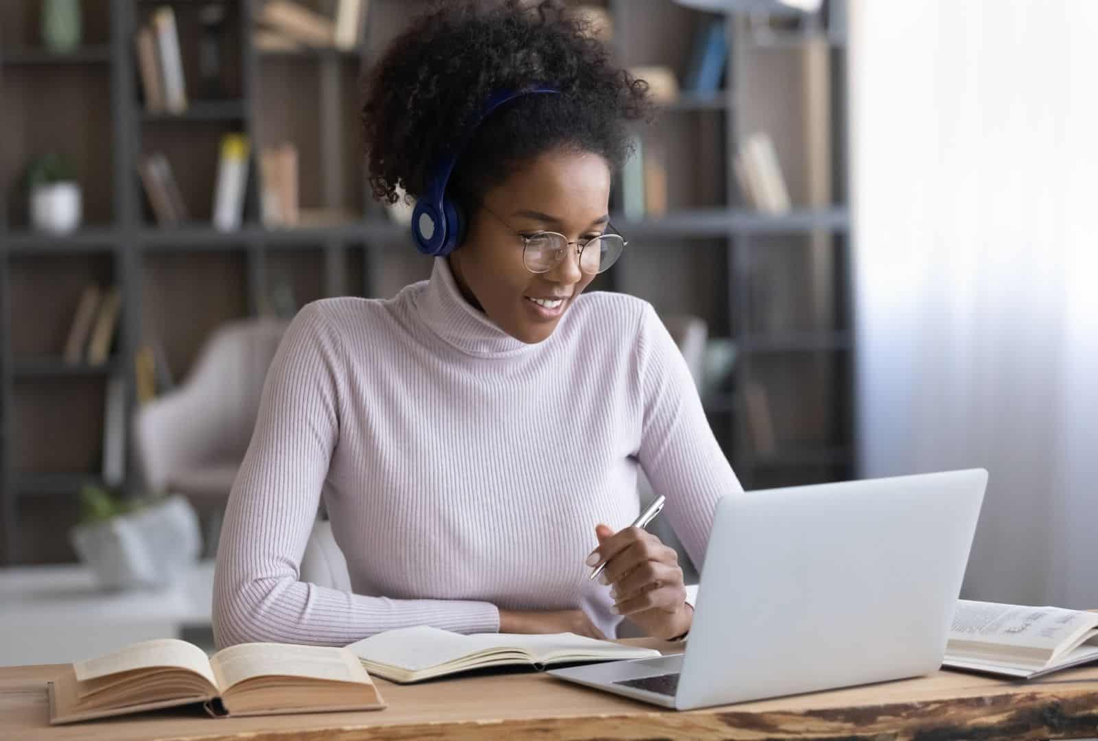 Female student with headphones and glasses actively participating in Hebrew Zoom Lessons on her laptop, with a notebook and textbook on the desk, illustrating focused online language learning.