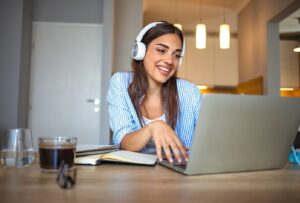 Woman wearing headphones studying Hebrew online at home with laptop and notebook on desk